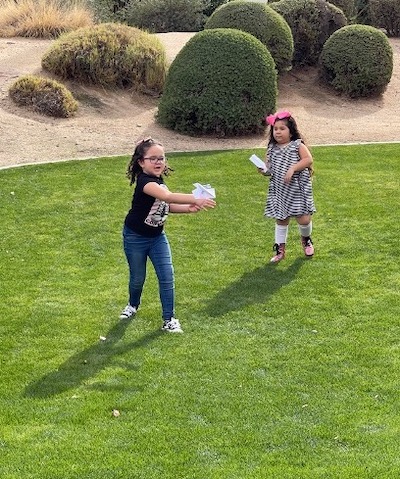Airplane_1 Two young girls playing with paper airplanes in a yard.