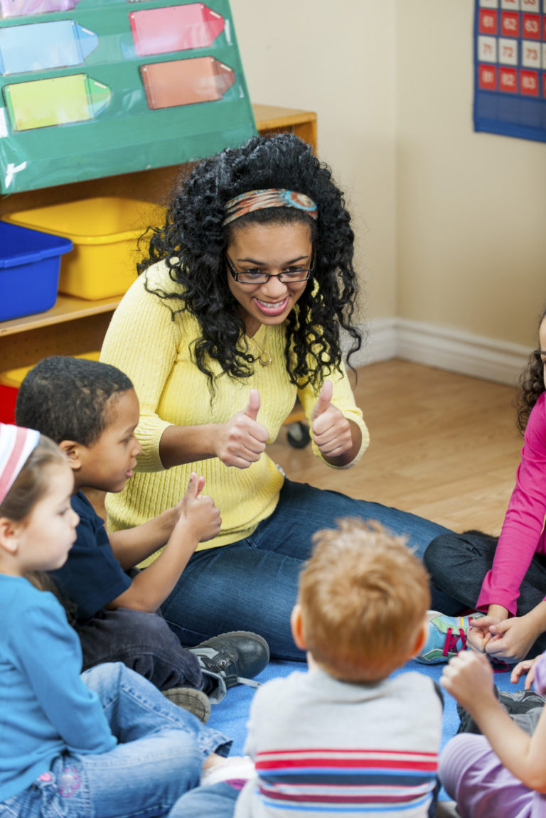 Group of kids in preschool. Teacher with excited expression sitting amongst a circle of children