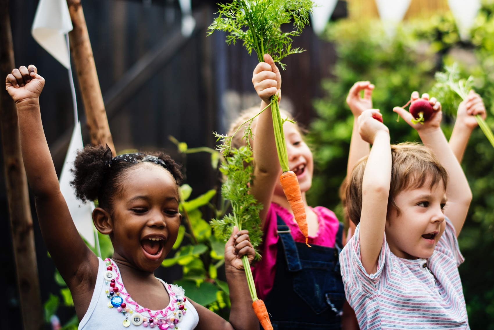 small children standing in a garden holding up just picked vegetables