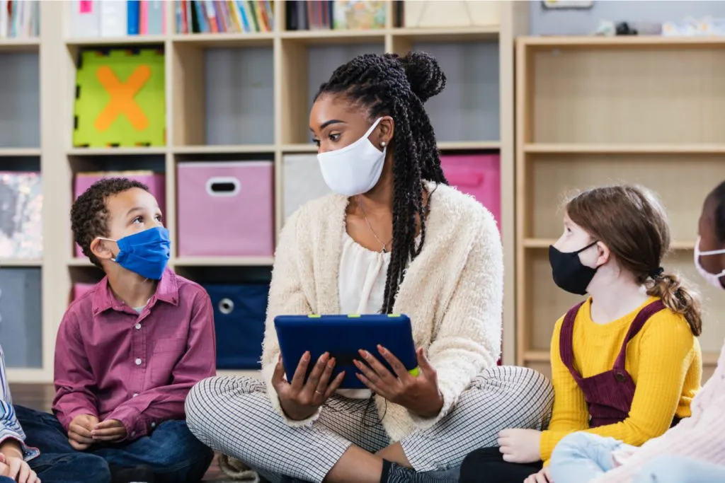 teacher reading to children in classroom while wearing masks