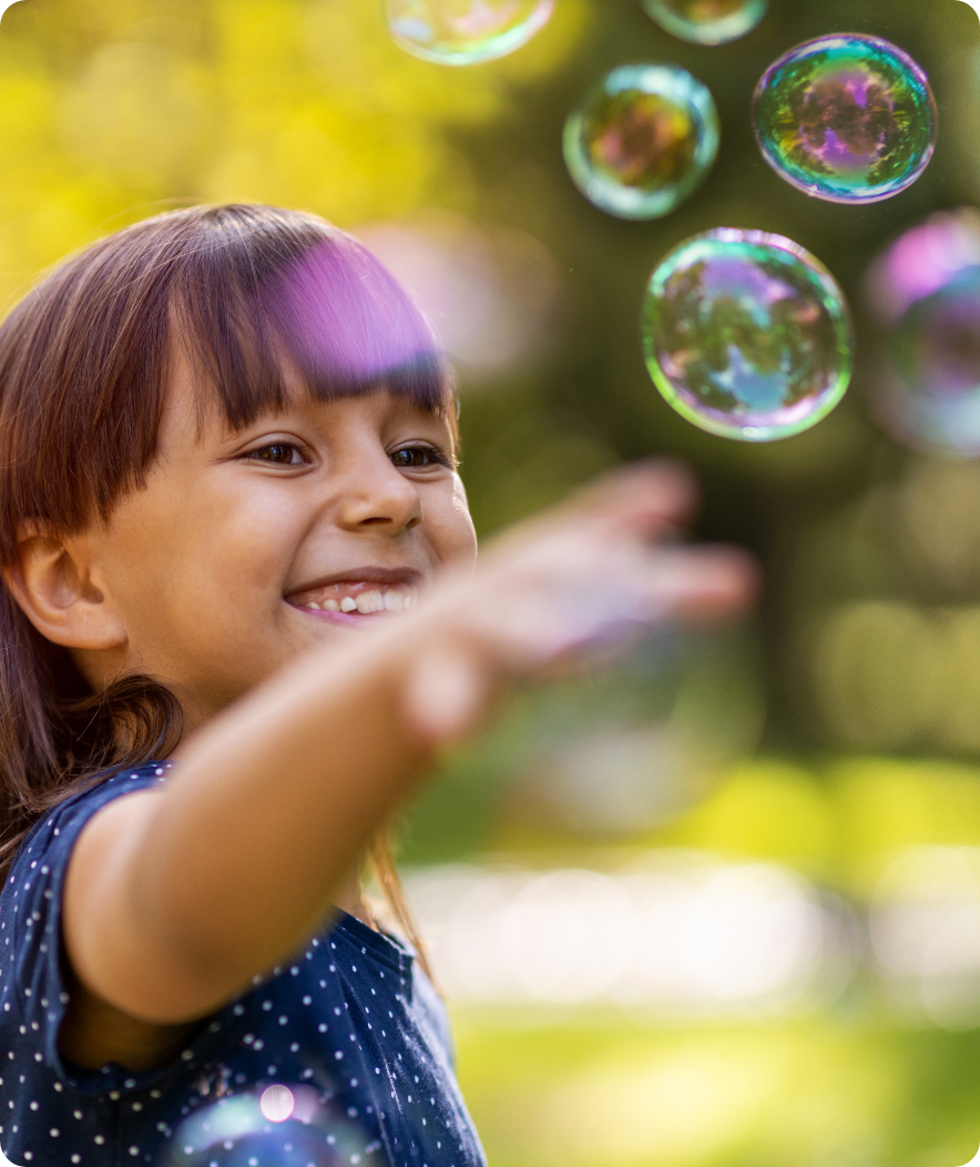 child outdoors playing with bubbles smiling