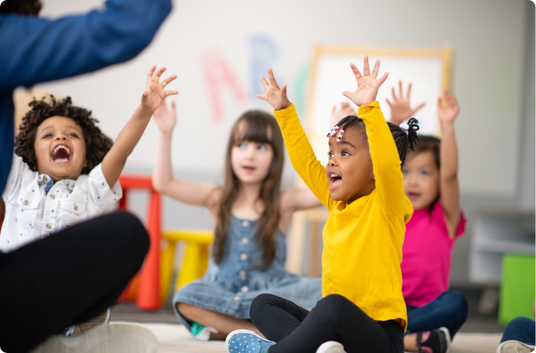 multiple happy children in a classroom hands raised singing