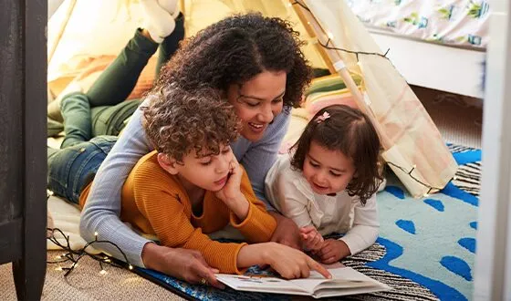 A mother and her two children reading together on the floor.