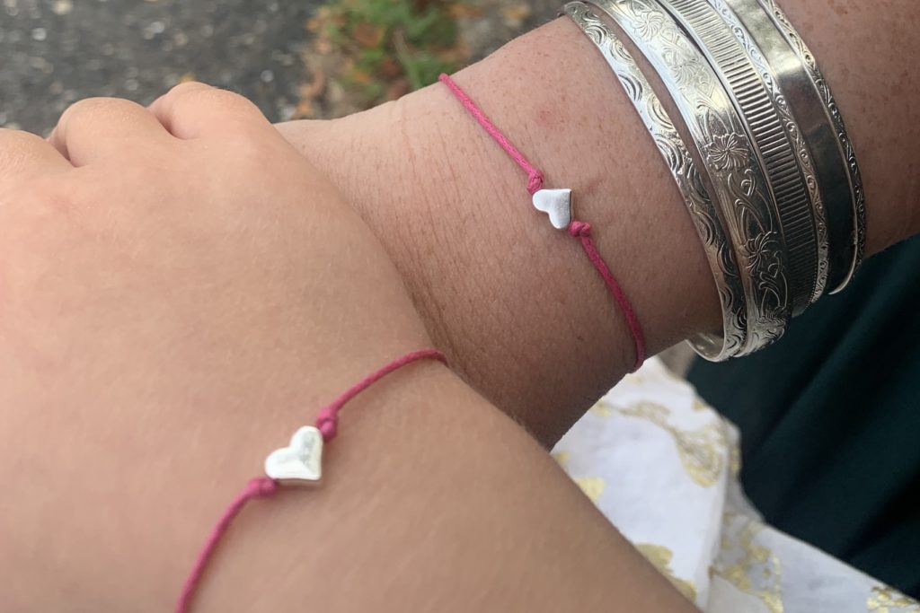 A close up of Lucy & her mama's hands, showing off their matching pink, heart bracelets.