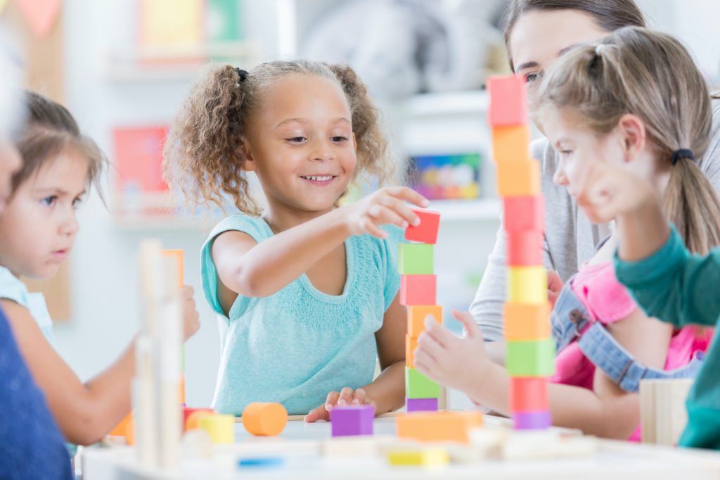 A young girl builds a block tower on a table