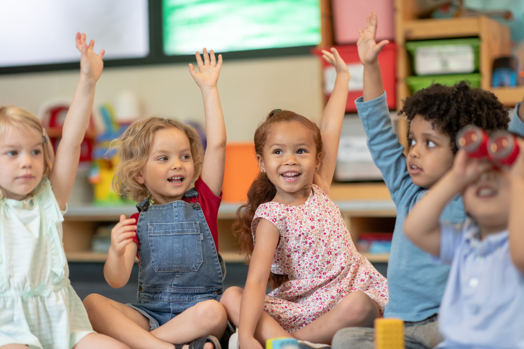 A group of preschool children raise their hand during large group time