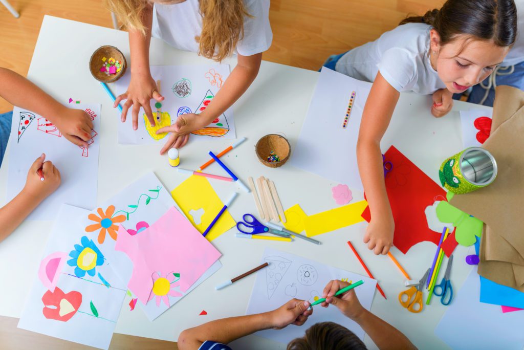 Children sit around a table, creating art from construction paper