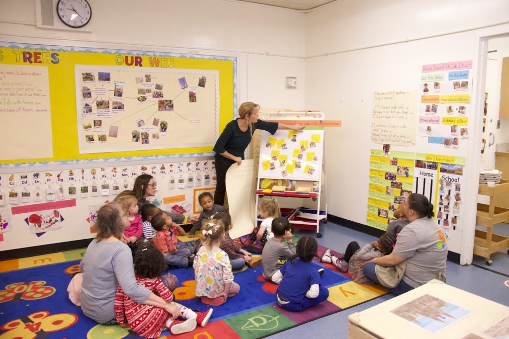 A teacher points to words as she reads off a chart during large group time