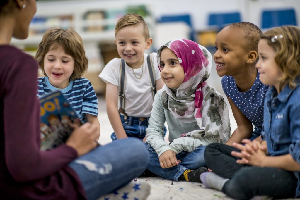 Children listen excitedly as their teacher reads them a book