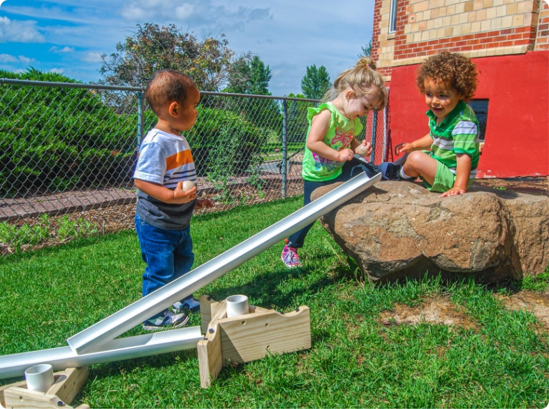 three children playing with ramps outdoors