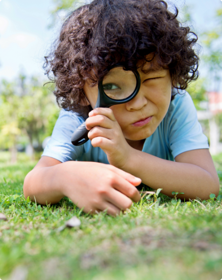 boy outdoor with magnifying glass investigating grass