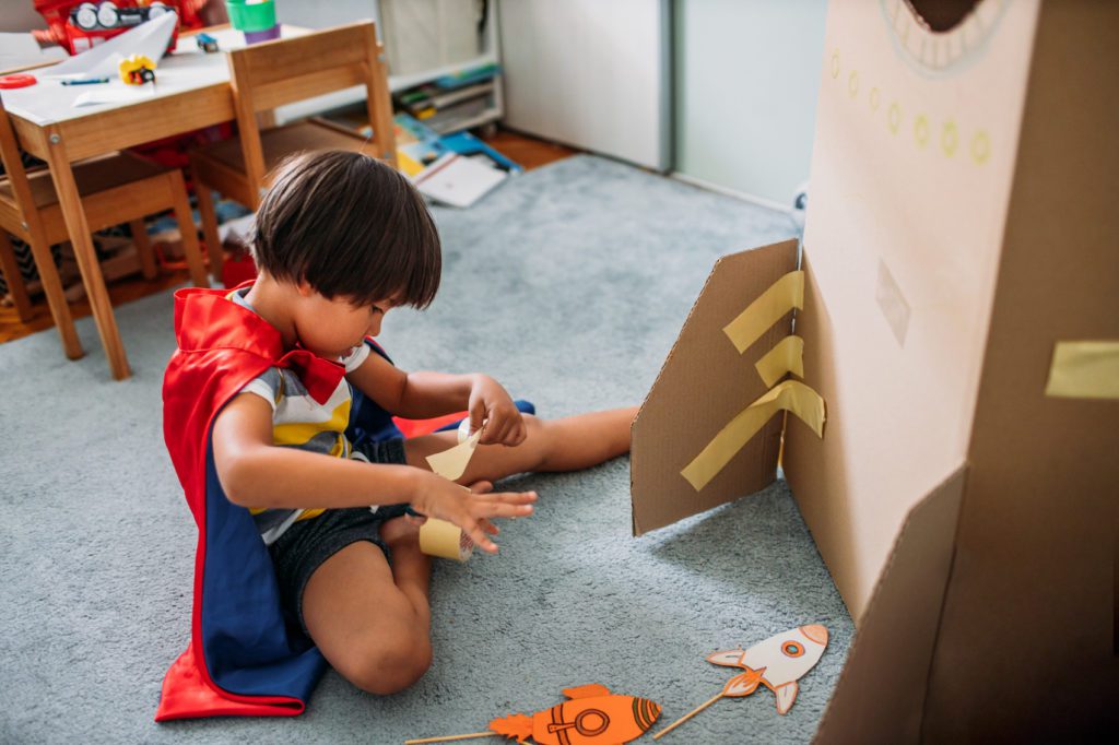 Boy Dressed Like A Superhero Playing With Cardboard Rocket