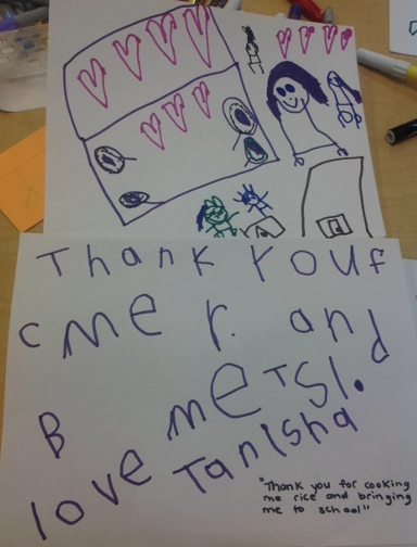 A handwritten note from a preschooler: “Thank you for cooking me rice and bringing me to school. Tanisha" with a drawing of her, her family, their kitchen, and hearts. 