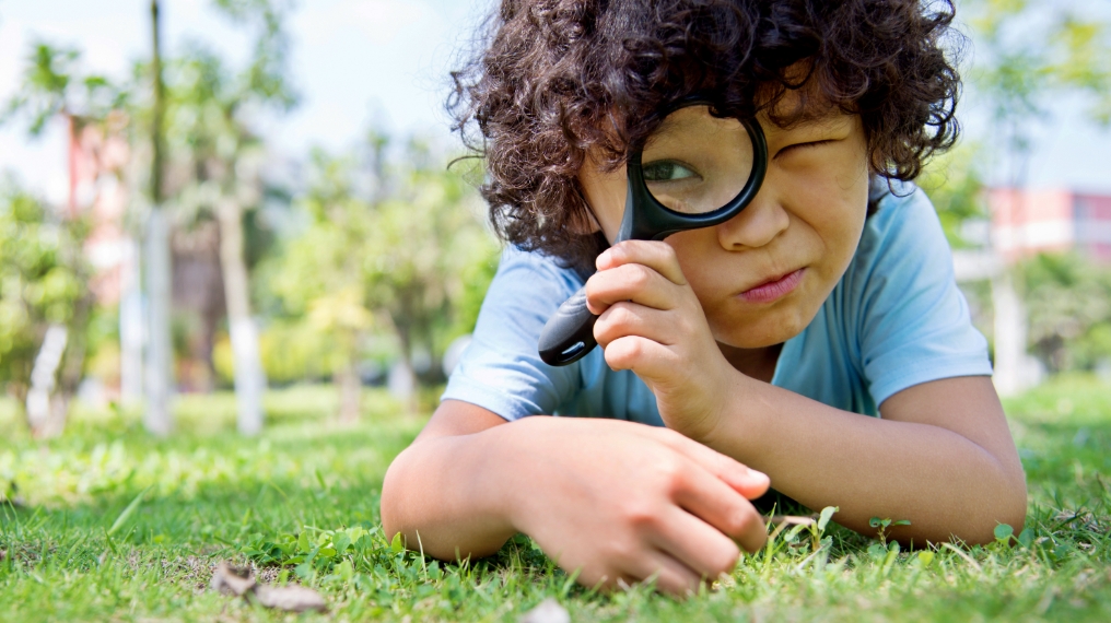 young boy outdoors with magnifying glass