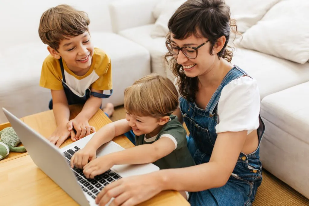 Mother and two sons play at laptop.