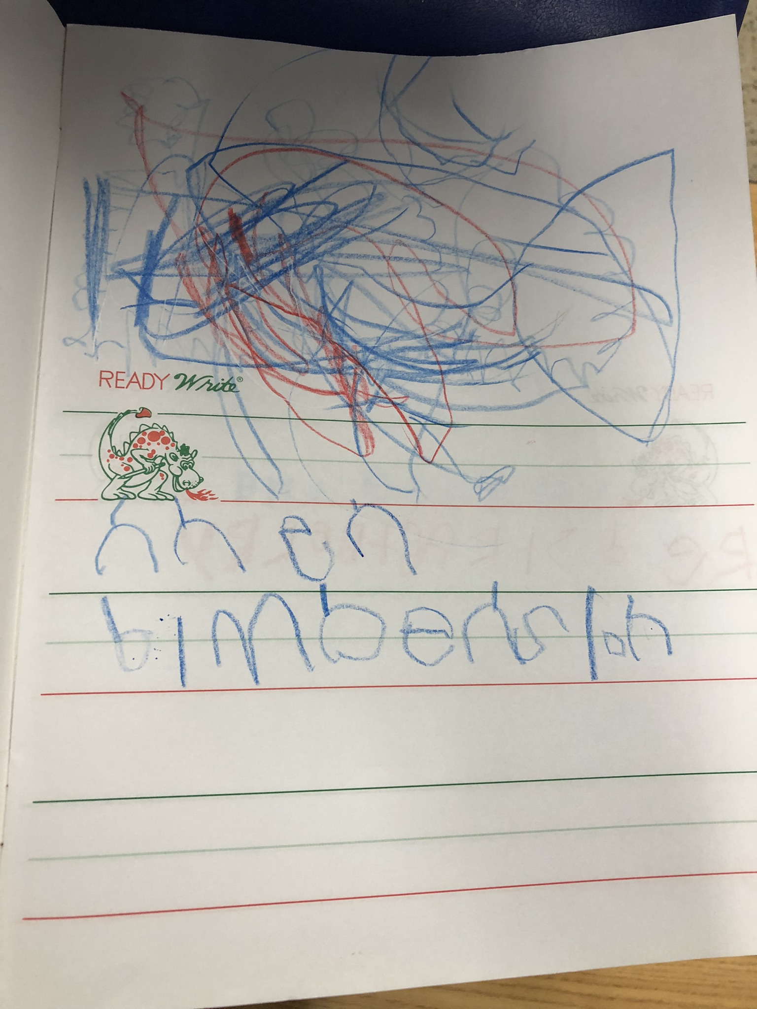 A child has begun forming the letters of their name on a piece of paper.