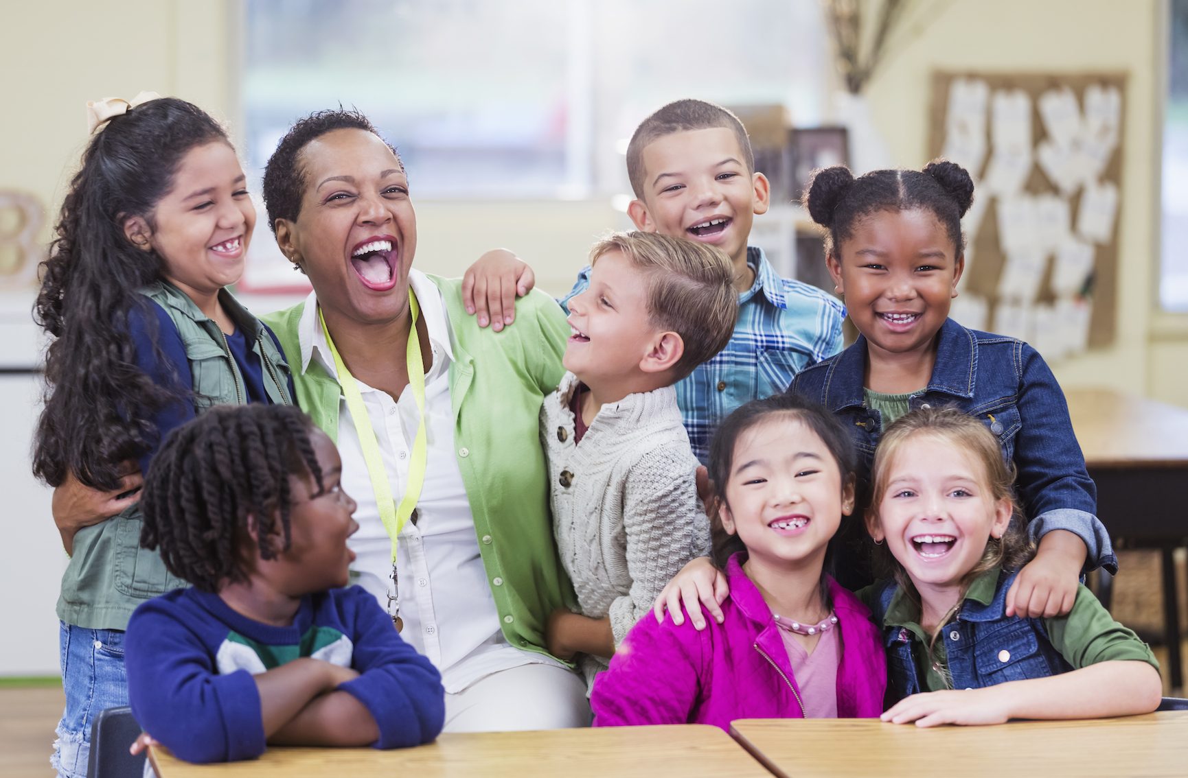 7 children surround and hug a happy teacher.