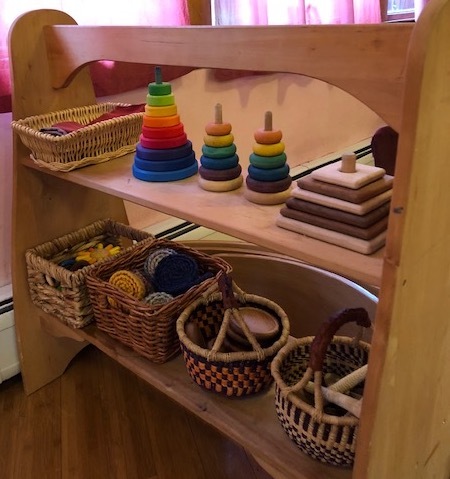 Wooden toys are arranged, spaced out, on a small wooden shelf, easily reachable by a small child. 