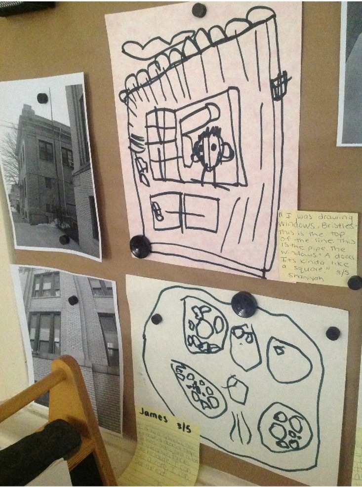 Children's Black & White Drawings of their school Building are displayed on a classroom wall. 