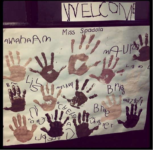 A sign reads "WELCOME" and is surrounded by children's handprints in different colors.