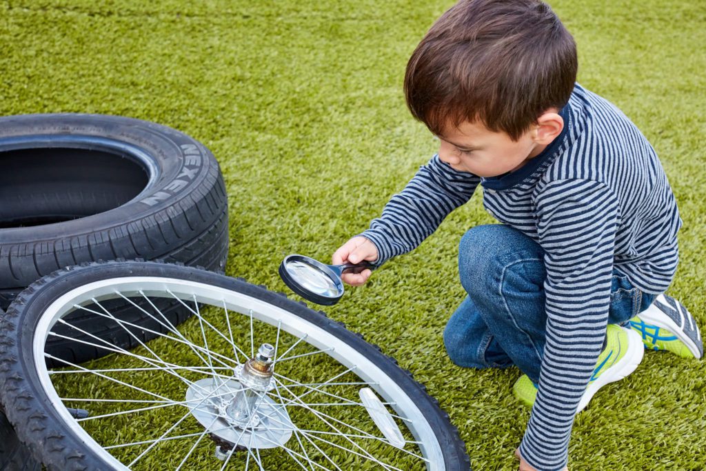 young boy with a magnifying glass examining a bike tire