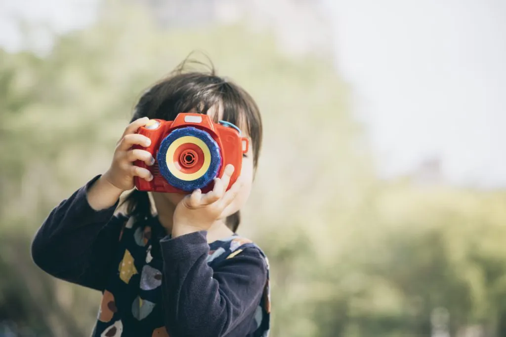 Preschool girl playing with toy camera outside.