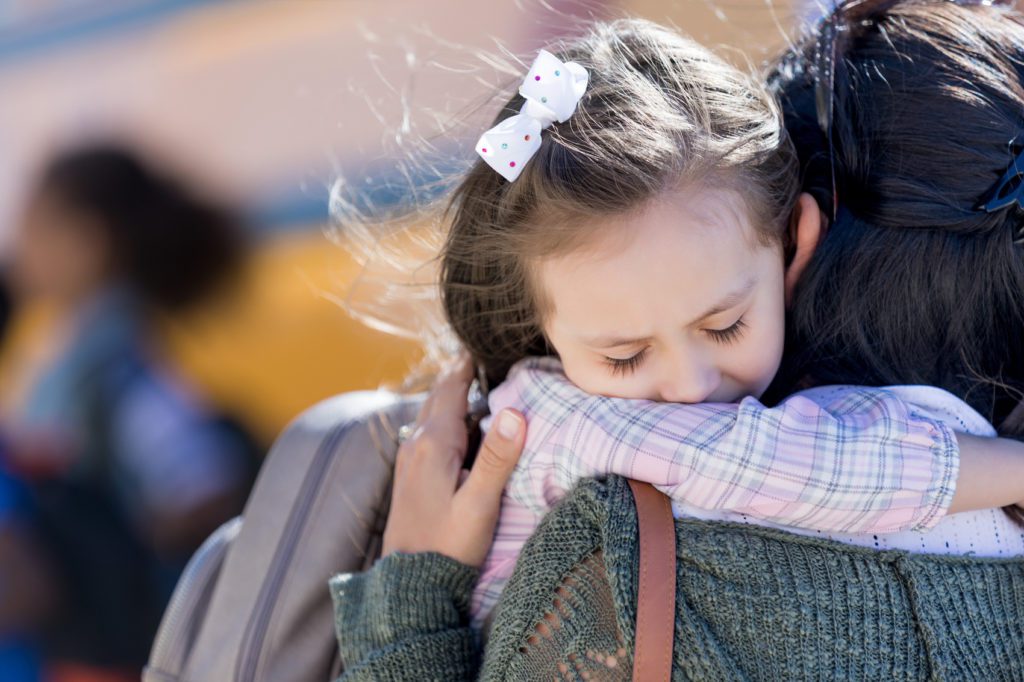 Worried little girl hugs her mom as she drops her off for school.