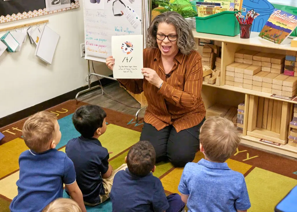 Teacher holding a letter card in front of a small group of students.