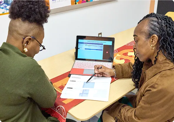 Two women sitting at a table looking at a piece of paper.