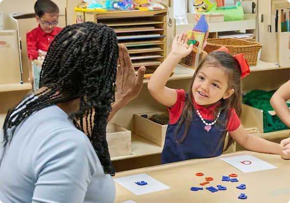 Teacher and child are high-fiving while sitting at a table