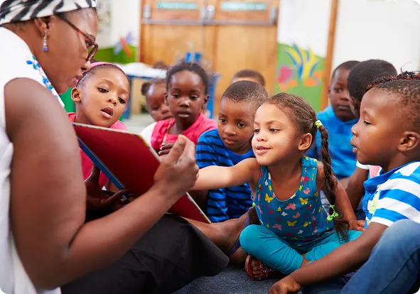 Children sitting around their teacher while she reads them a book